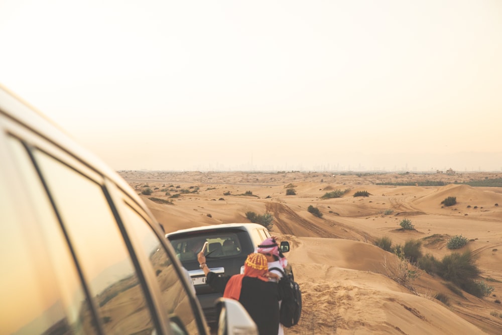 a group of people standing next to a car in the desert