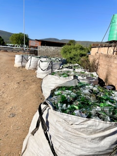 a bunch of bags filled with bottles sitting on top of a dirt field