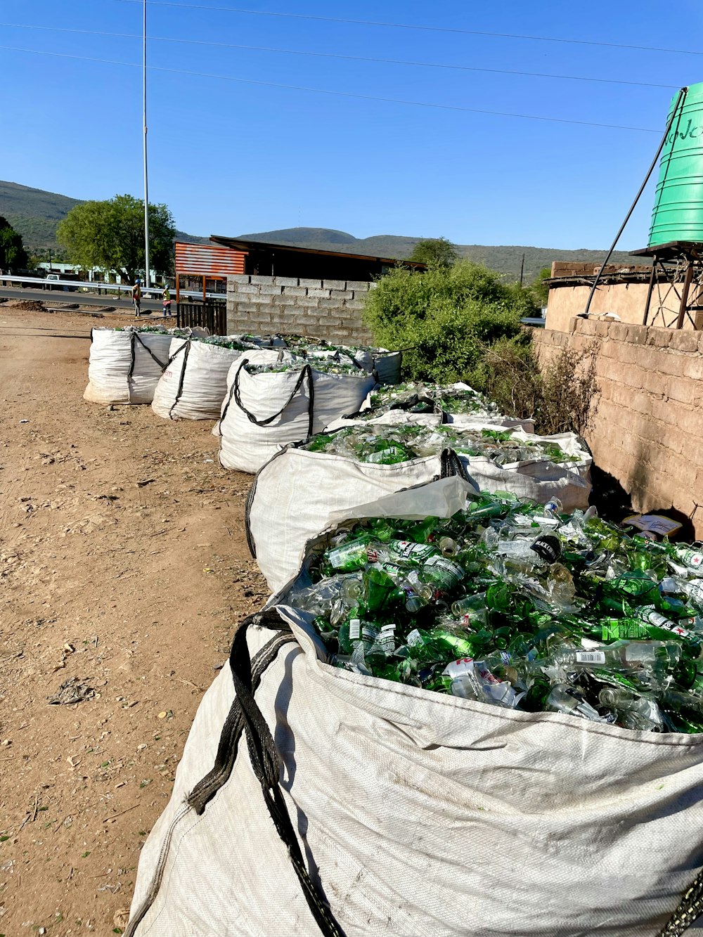 a bunch of bags filled with bottles sitting on top of a dirt field