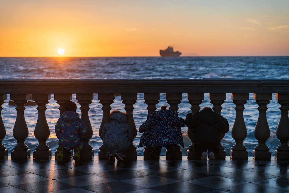 a group of children sitting on a bench watching the sun set