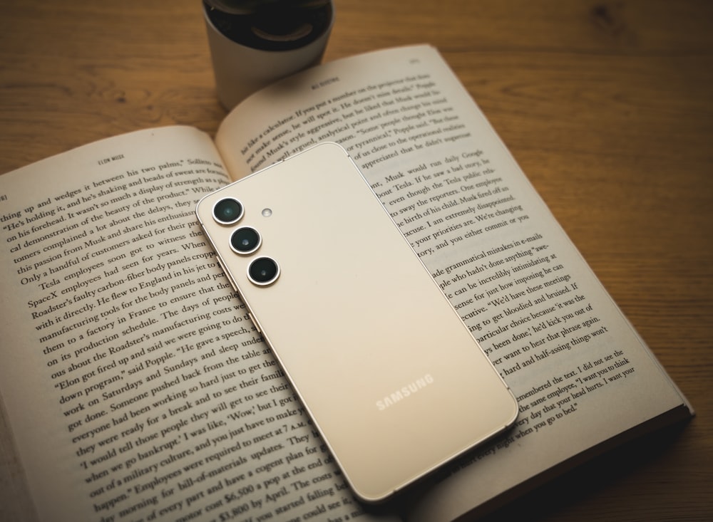 a white samsung phone sitting on top of an open book