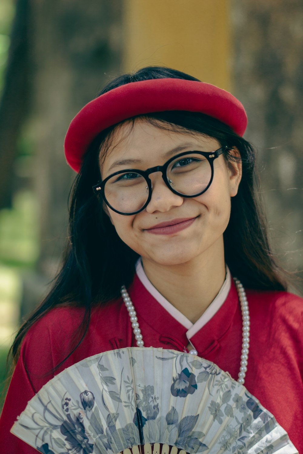 a young girl wearing glasses and a red hat holding a fan