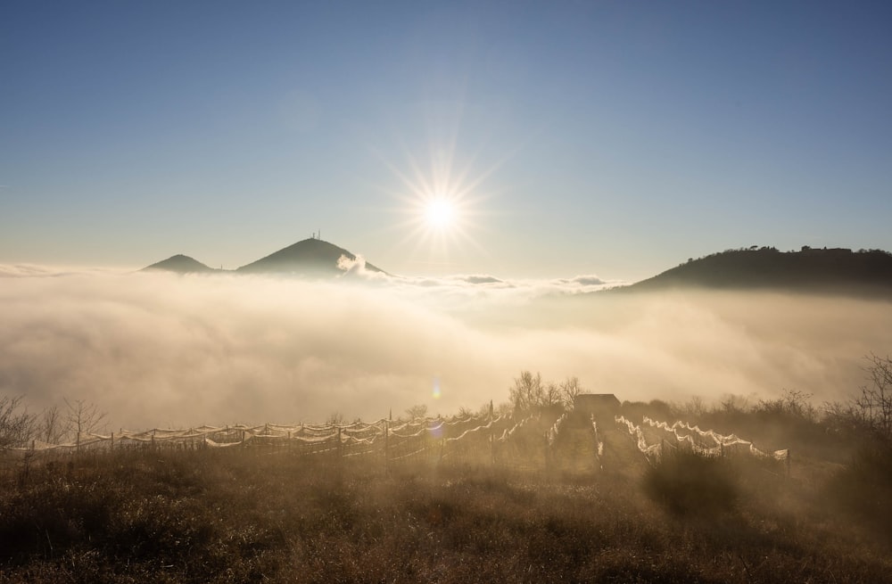the sun is shining over a foggy mountain
