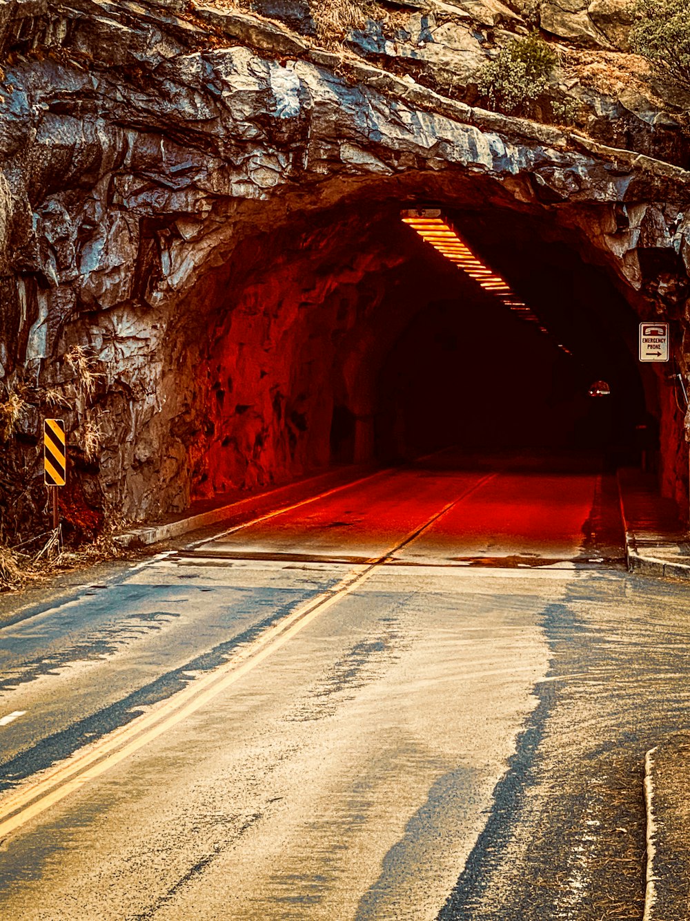 une route qui s’enfonce dans un tunnel avec un feu rouge au bout