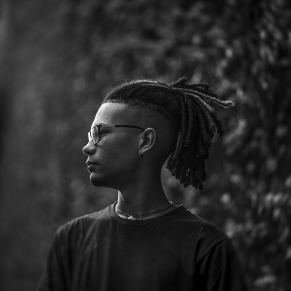 a man with dreadlocks standing in front of a tree