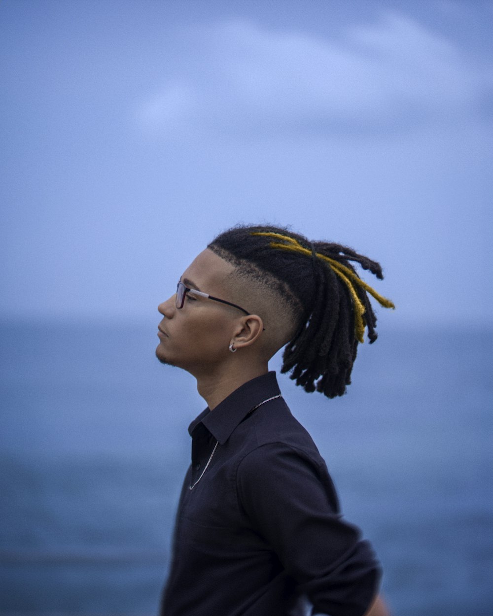 a man with dreadlocks standing in front of the ocean