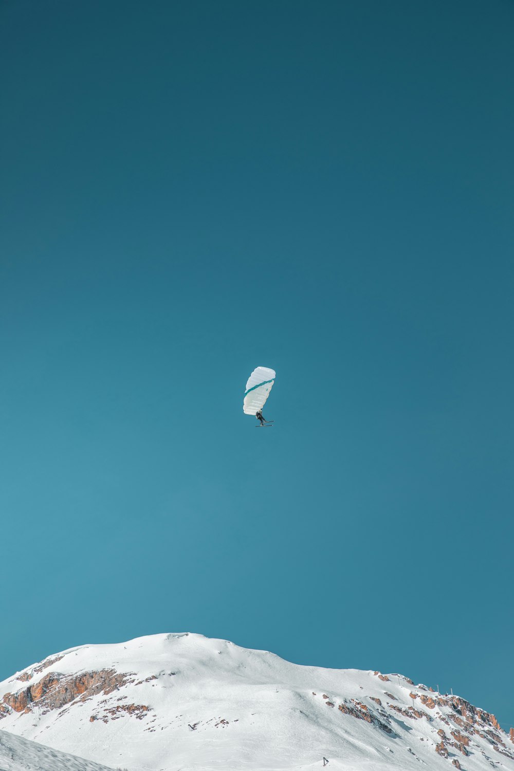 una cometa volando sobre una montaña cubierta de nieve bajo un cielo azul