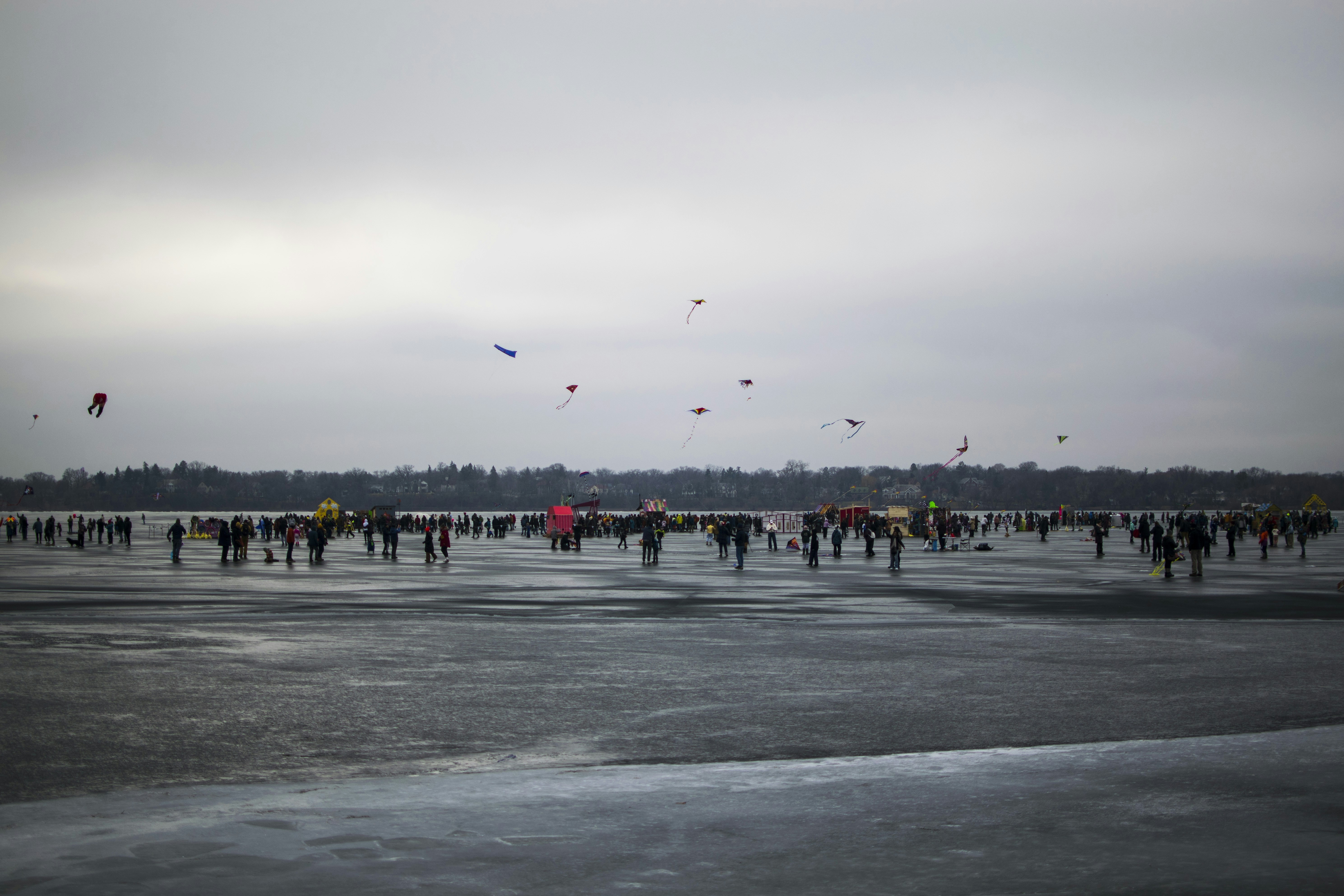 a group of people flying kites on top of a frozen lake, Minneapolis Winter Kite Festival 2024