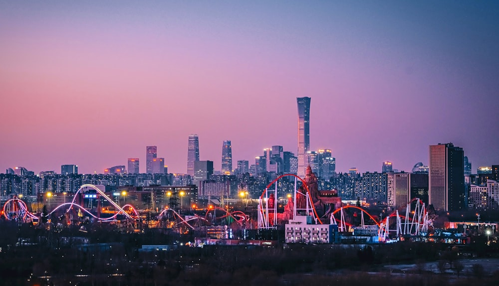 a city skyline with a roller coaster at dusk