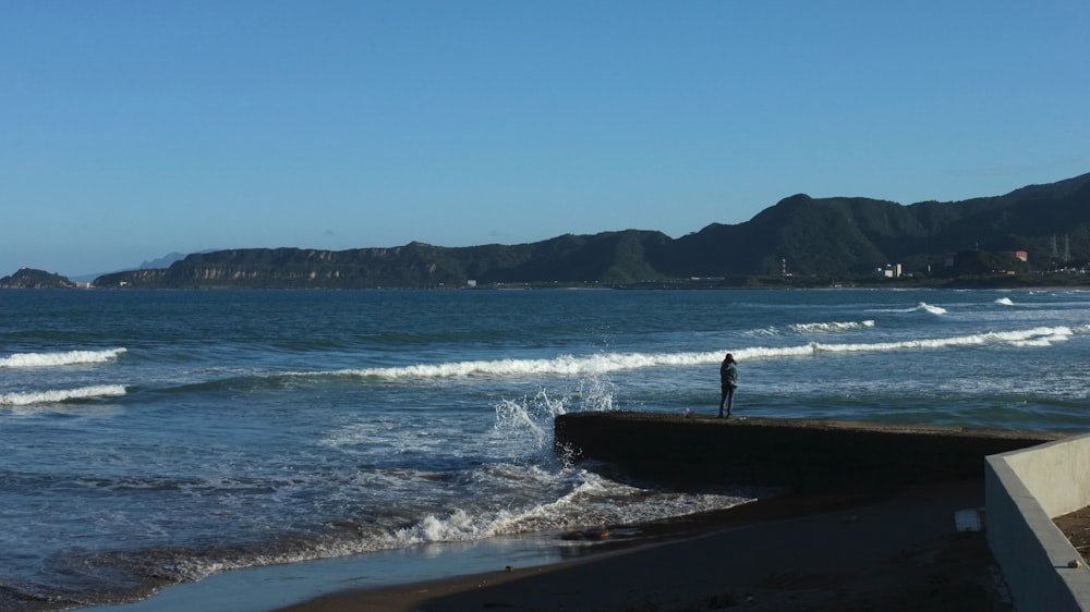 una persona in piedi su una spiaggia vicino all'oceano
