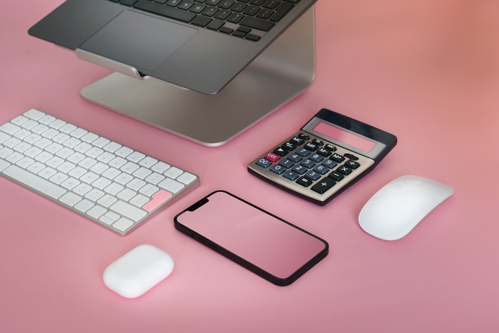 a calculator, keyboard, mouse and cell phone on a pink surface
