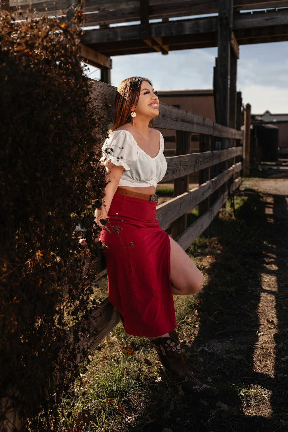 a woman leaning against a fence wearing a white top and red skirt