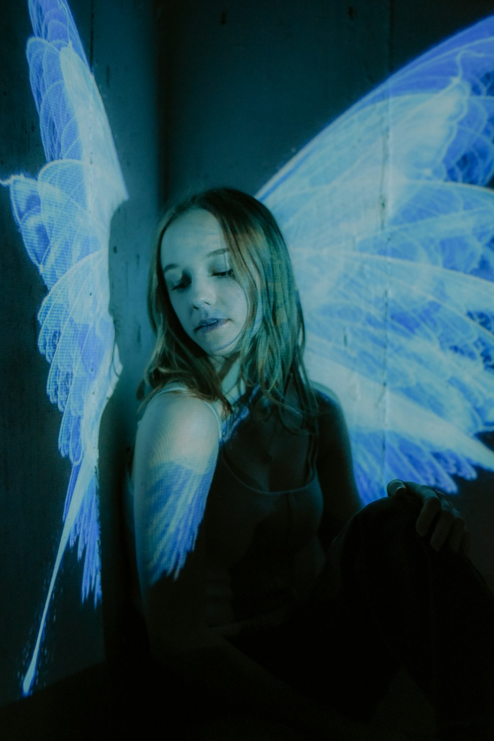 a woman with blue wings sitting in a dark room
