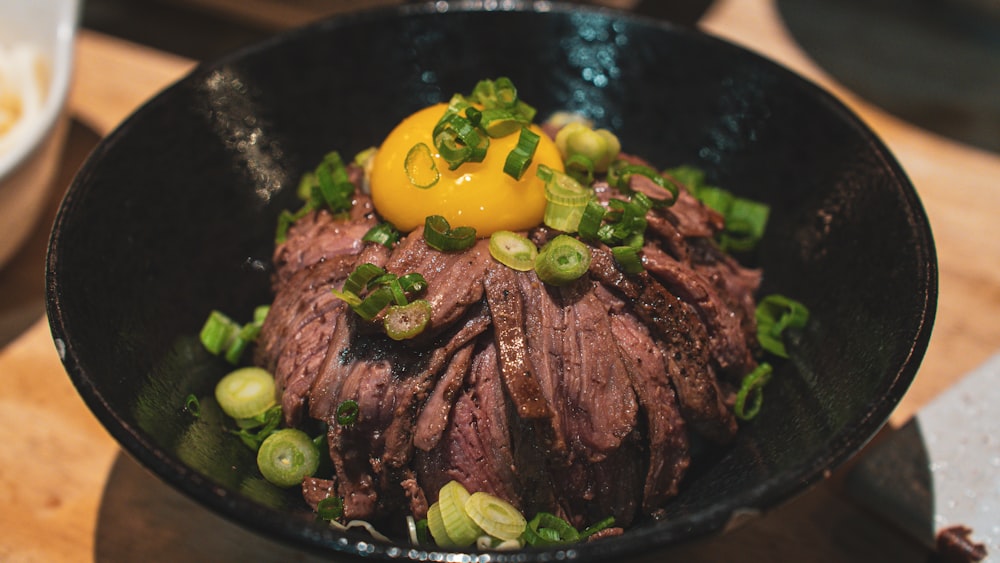 a black bowl filled with meat and vegetables