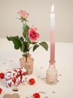 a pink rose in a vase next to a candle