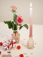 a pink rose in a vase next to a candle