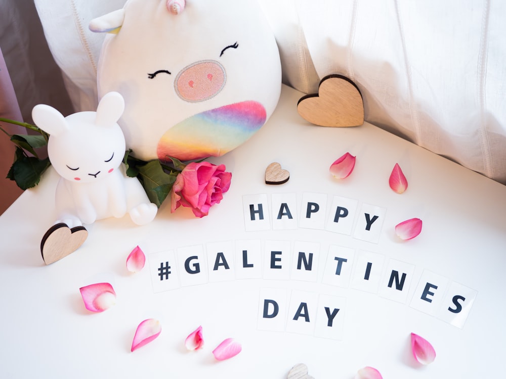 a white table topped with a white stuffed animal next to a pink rose