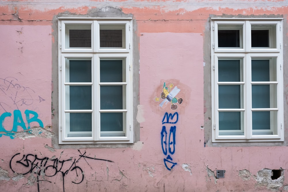 a pink building with white windows and graffiti on it