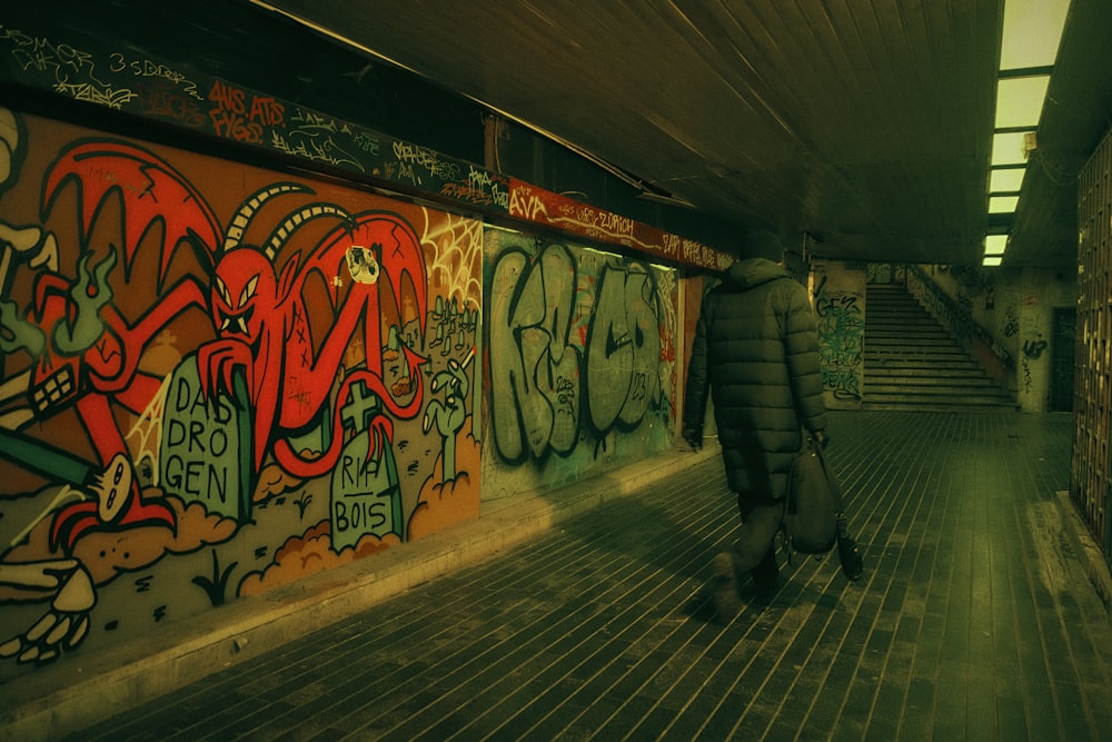 a person walking down a hallway with graffiti on the walls