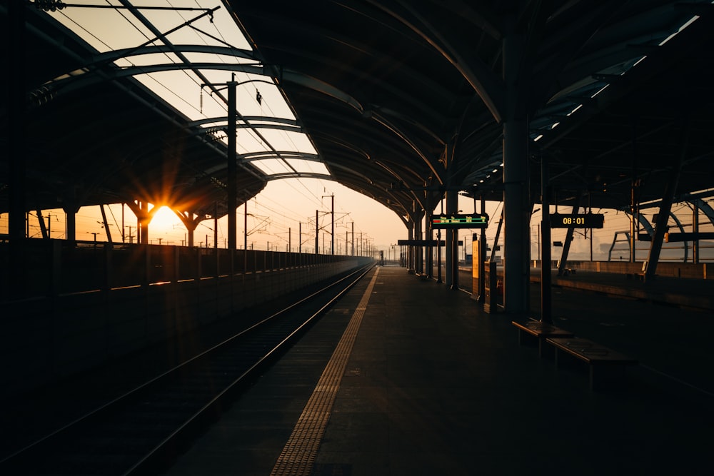 a train station with the sun setting in the background