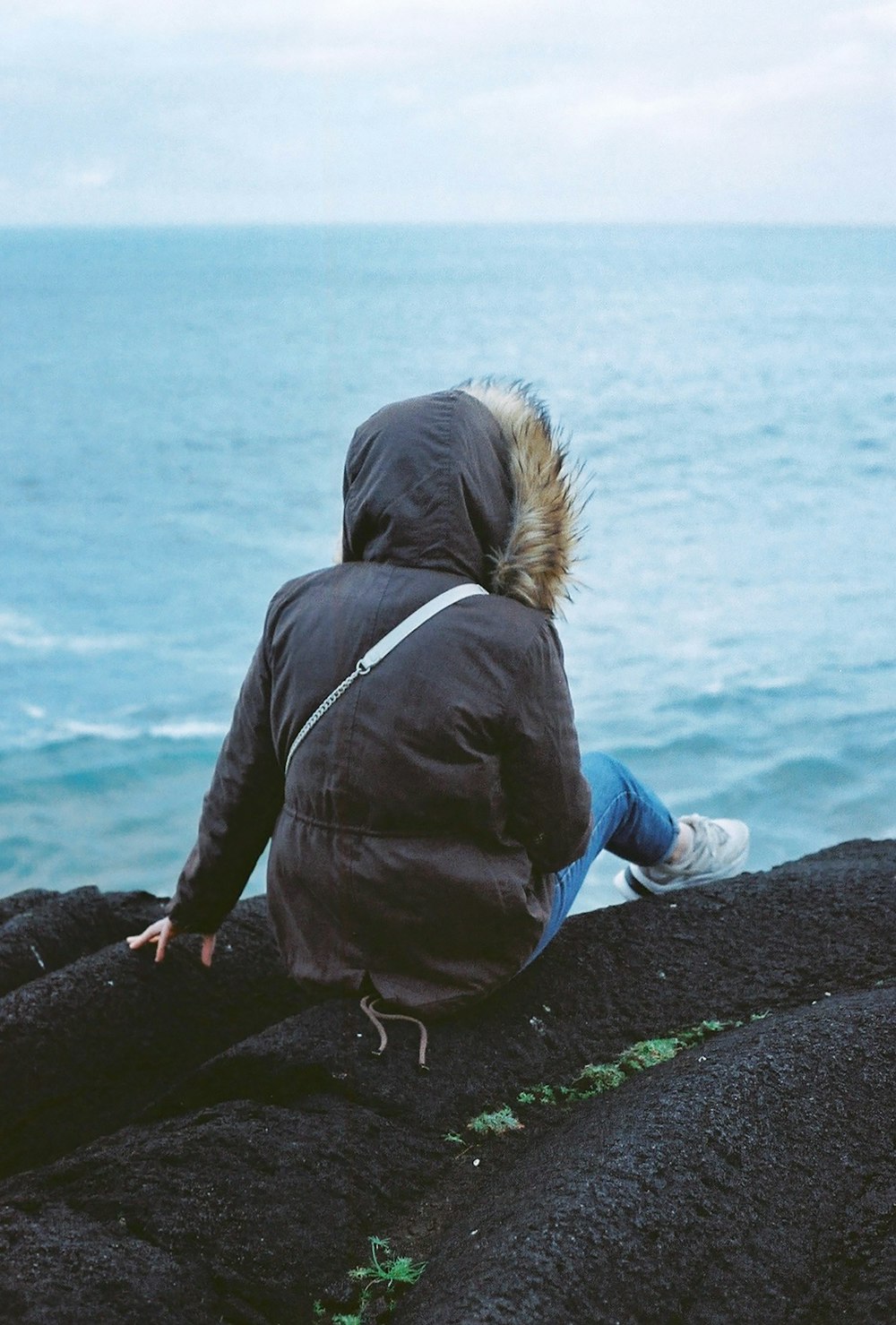 eine Person, die auf einem Felsen sitzt und auf das Meer blickt