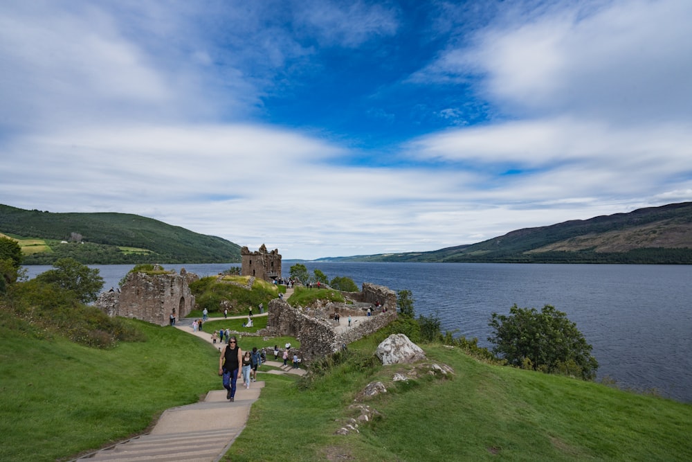 a group of people walking up a hill next to a body of water