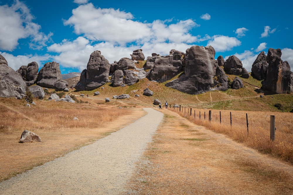 a dirt road in a field with large rocks in the background