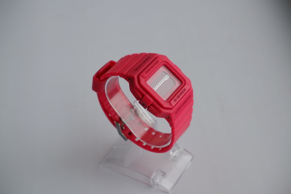 a red watch sitting on top of a plastic stand