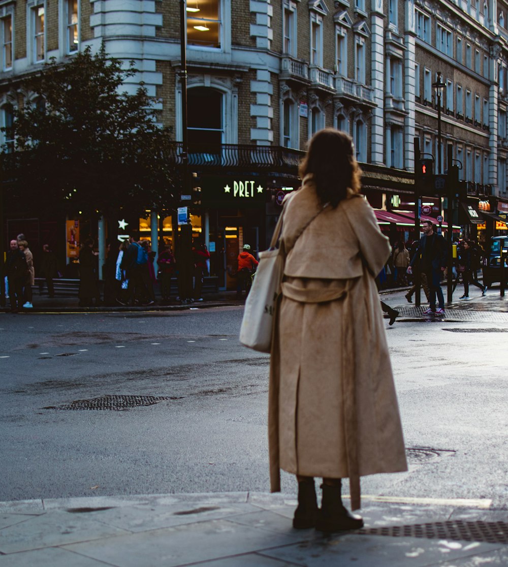 a woman in a trench coat standing on a street corner