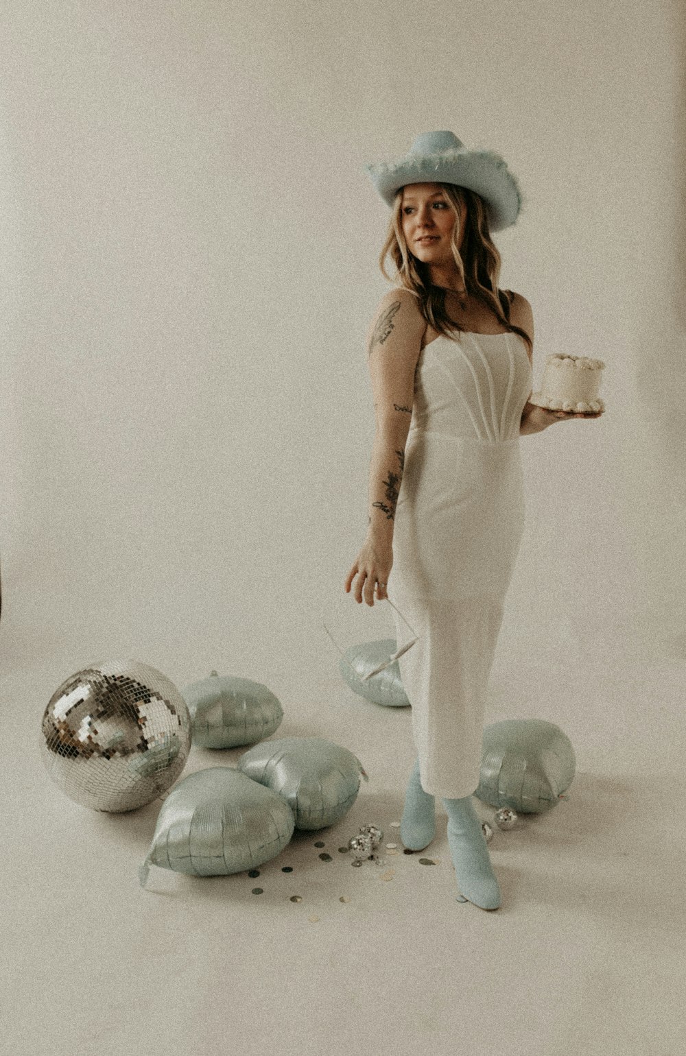 a woman in a white dress and hat holding a cake