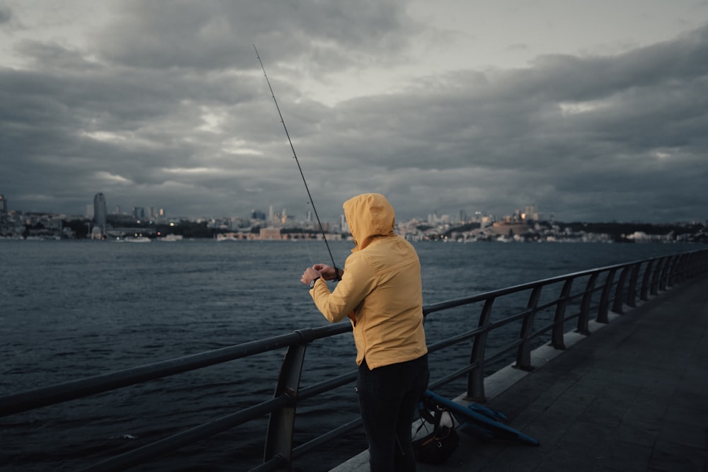 a person standing on a pier fishing on a cloudy day