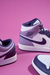 a pair of purple and white sneakers on a pink background