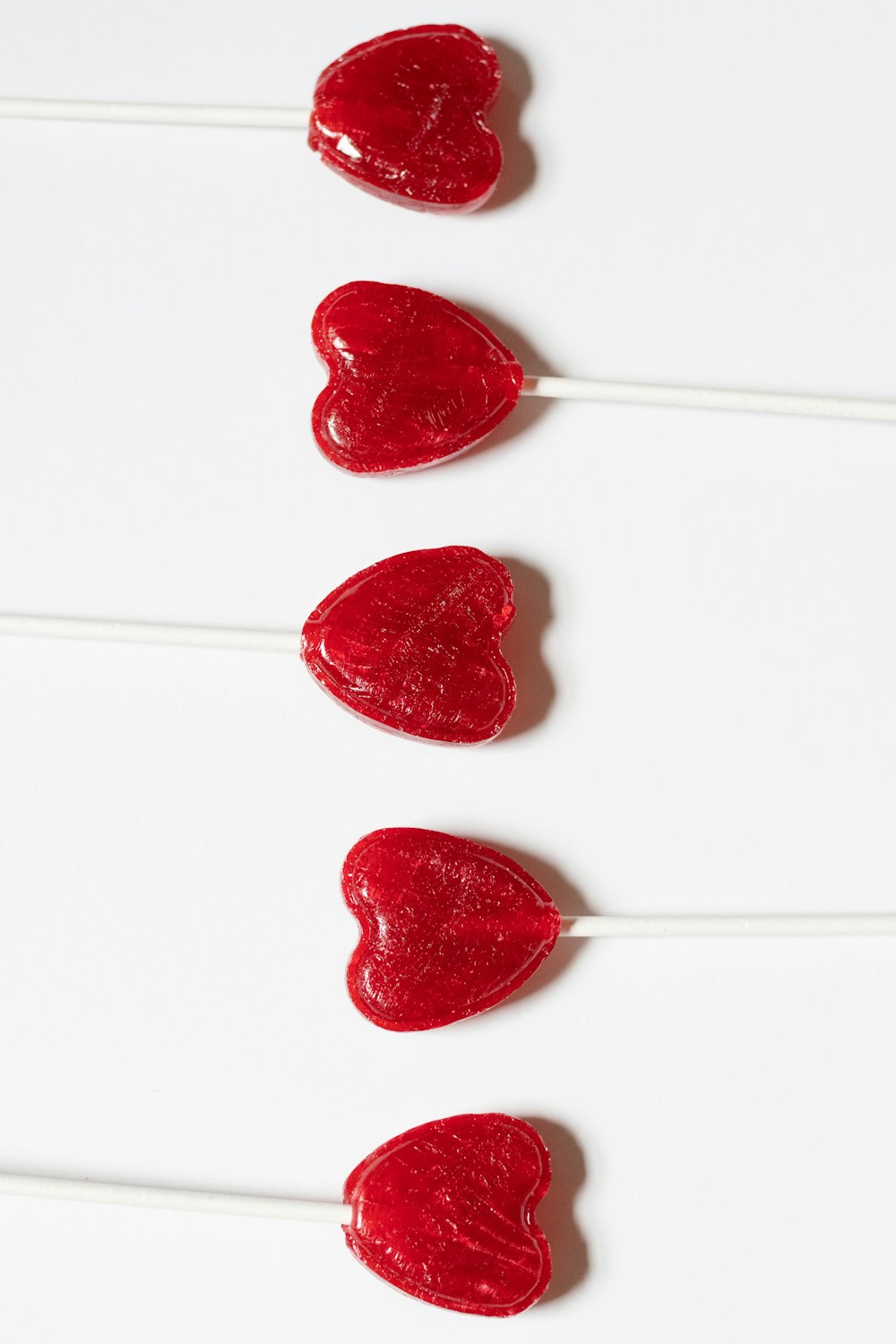 Tres piruletas en forma de corazón sobre una superficie blanca