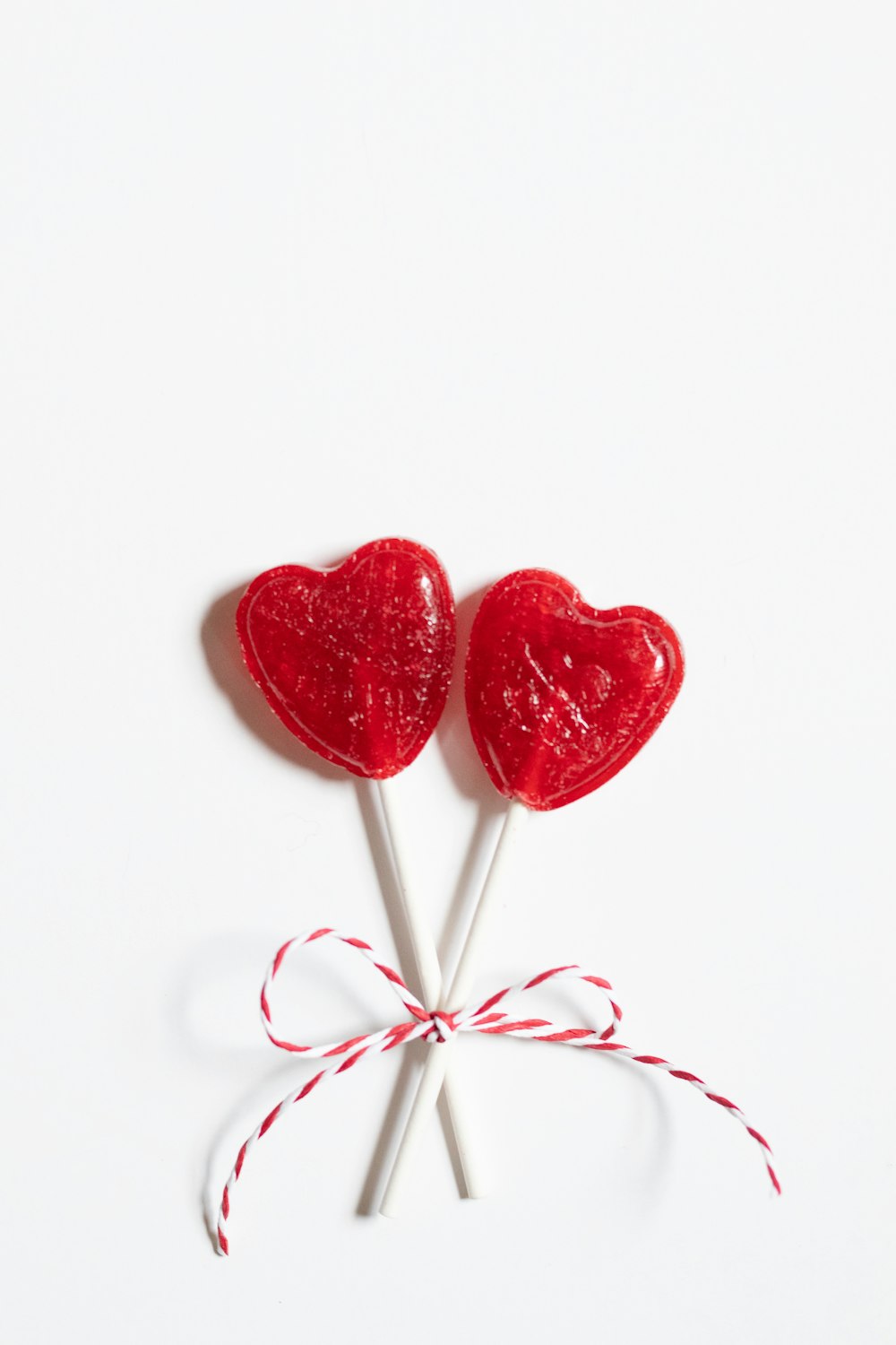 two heart shaped lollipops tied up on a white surface