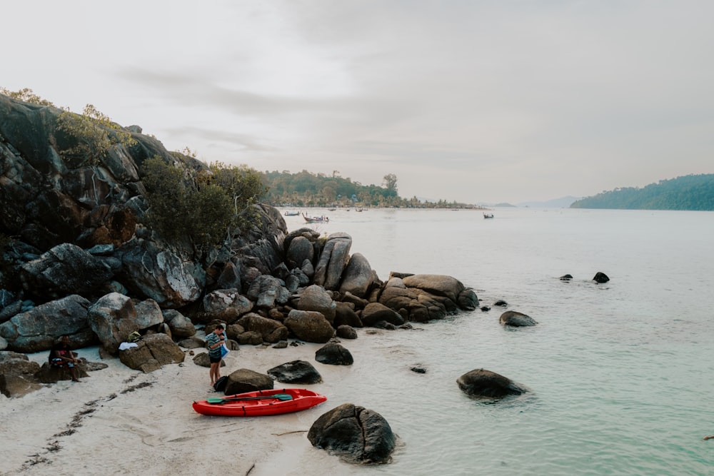 a man standing on a beach next to a red kayak