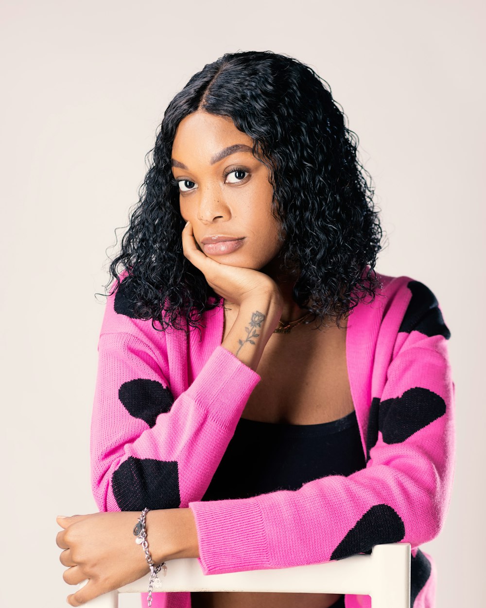 a woman in a pink cardigan leaning on a chair