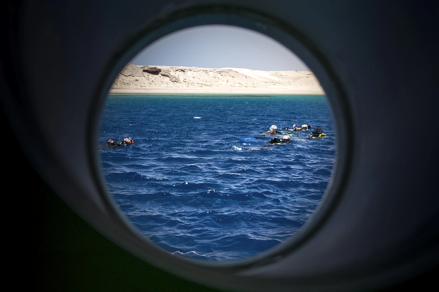 The sea and swimmers seen through the round porthole of a boat's cabin