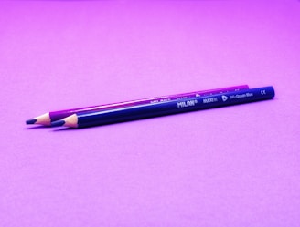 a purple pencil sitting on top of a pink surface