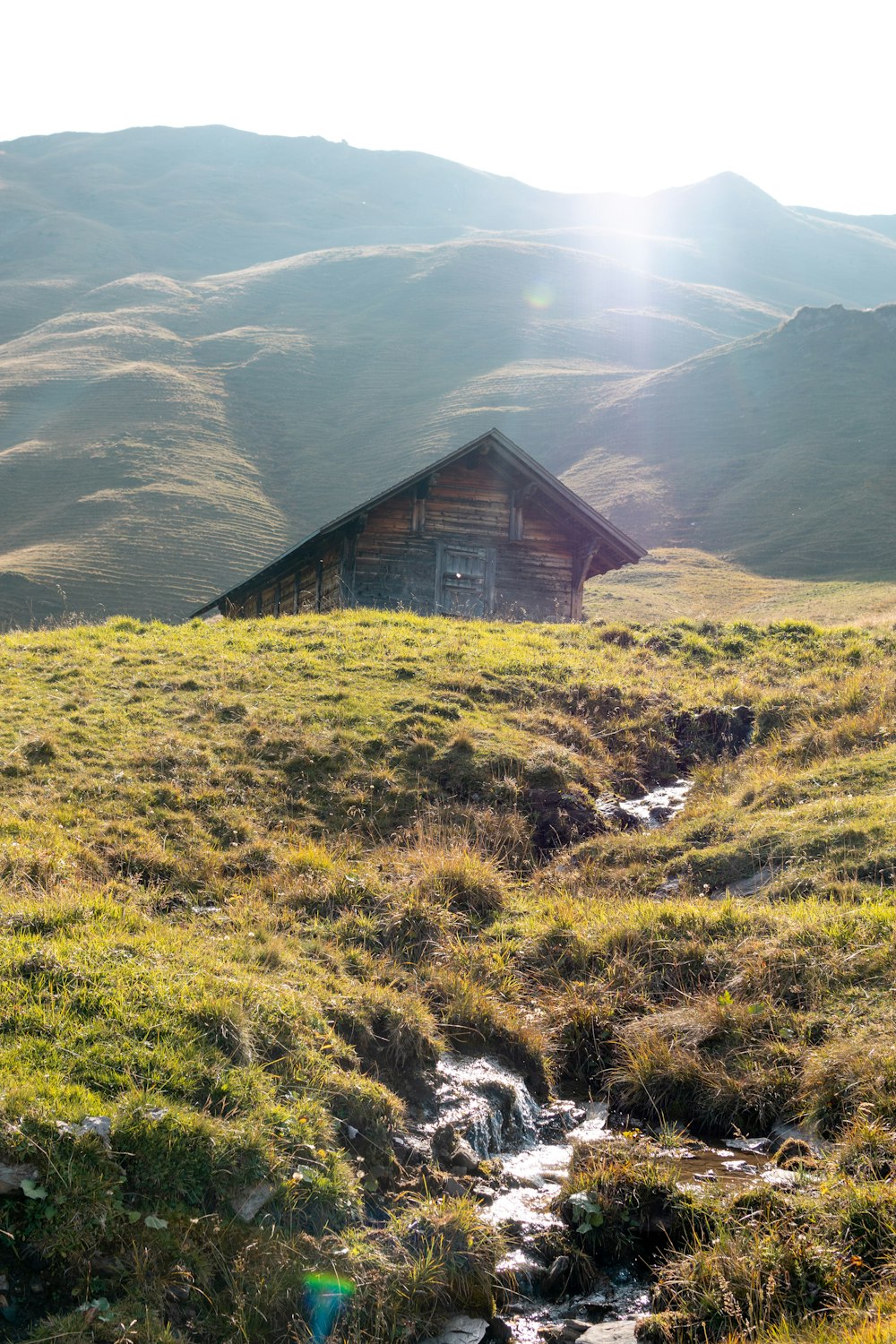 a small cabin on a grassy hill with a stream running through it