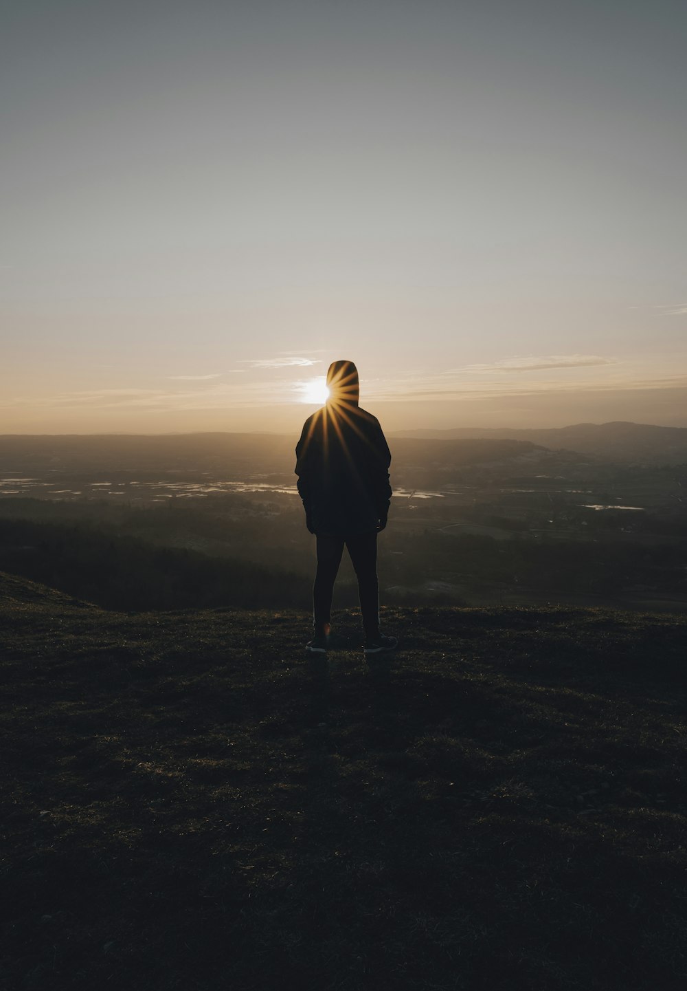 eine Person, die bei Sonnenuntergang auf einem Hügel steht