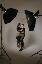 a man and woman sitting on a stool in front of a camera
