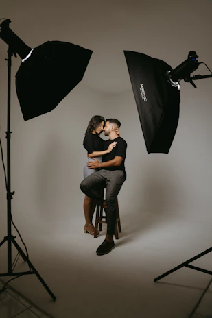 a man and woman sitting on a stool in front of a camera