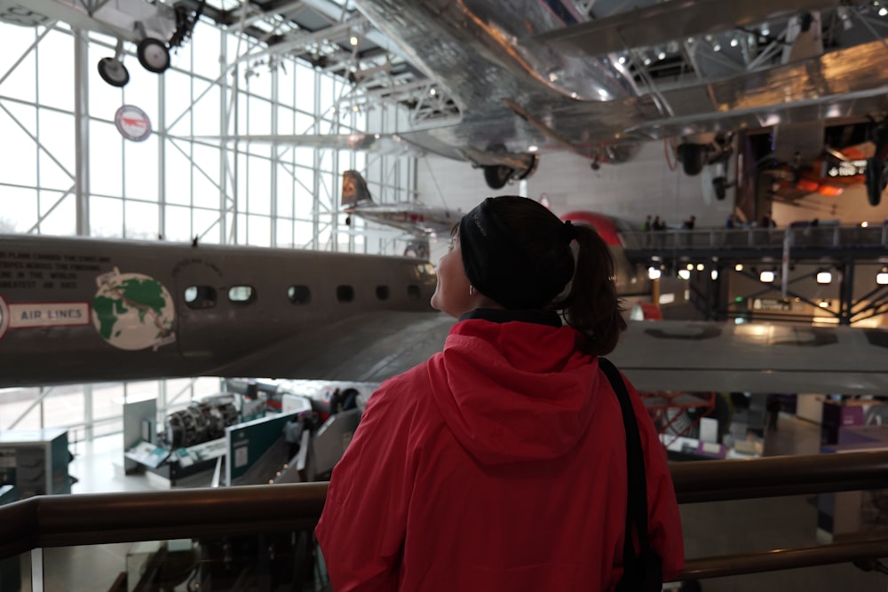 a woman in a red jacket looking at a plane