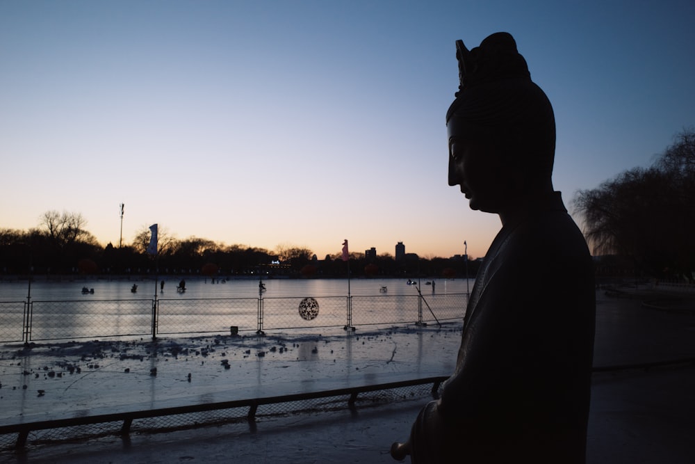 a statue of a person standing in front of a body of water