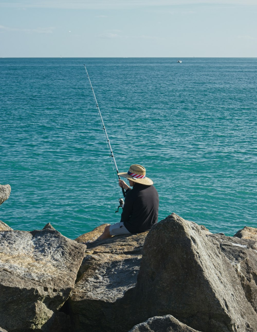 a man sitting on a rock fishing on the ocean
