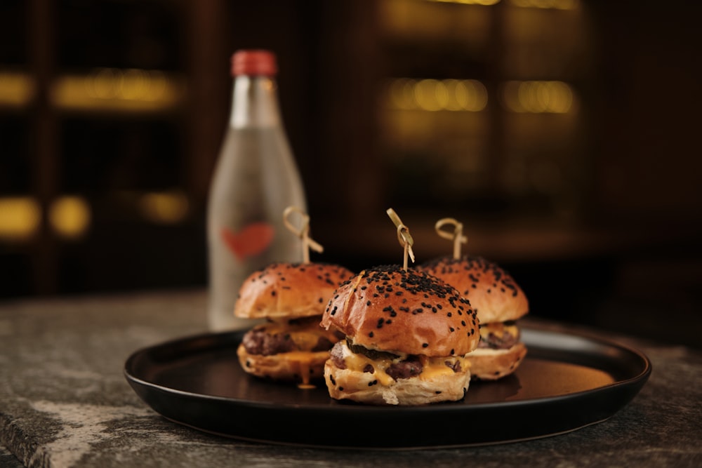 a black plate topped with two hamburgers next to a bottle