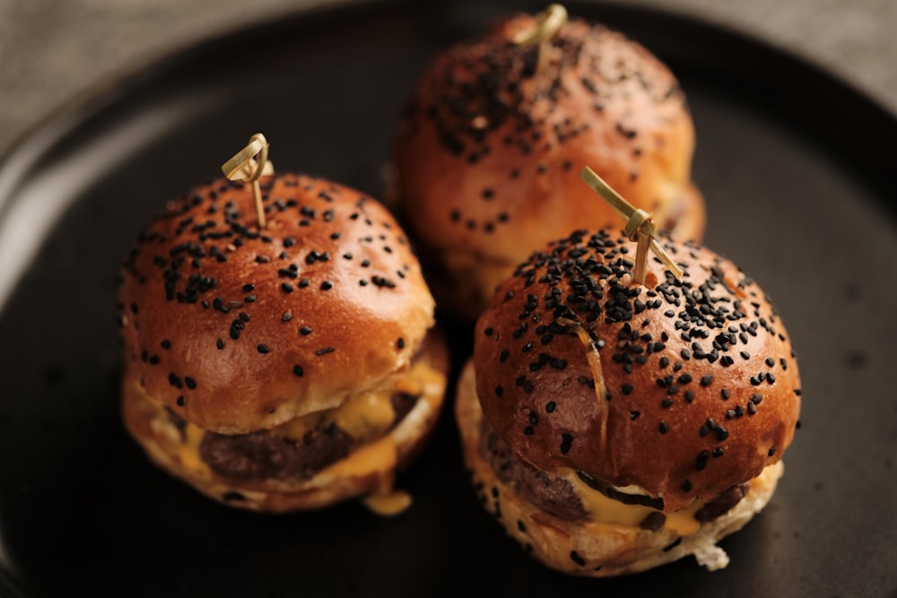 three mini burgers on a black plate on a table