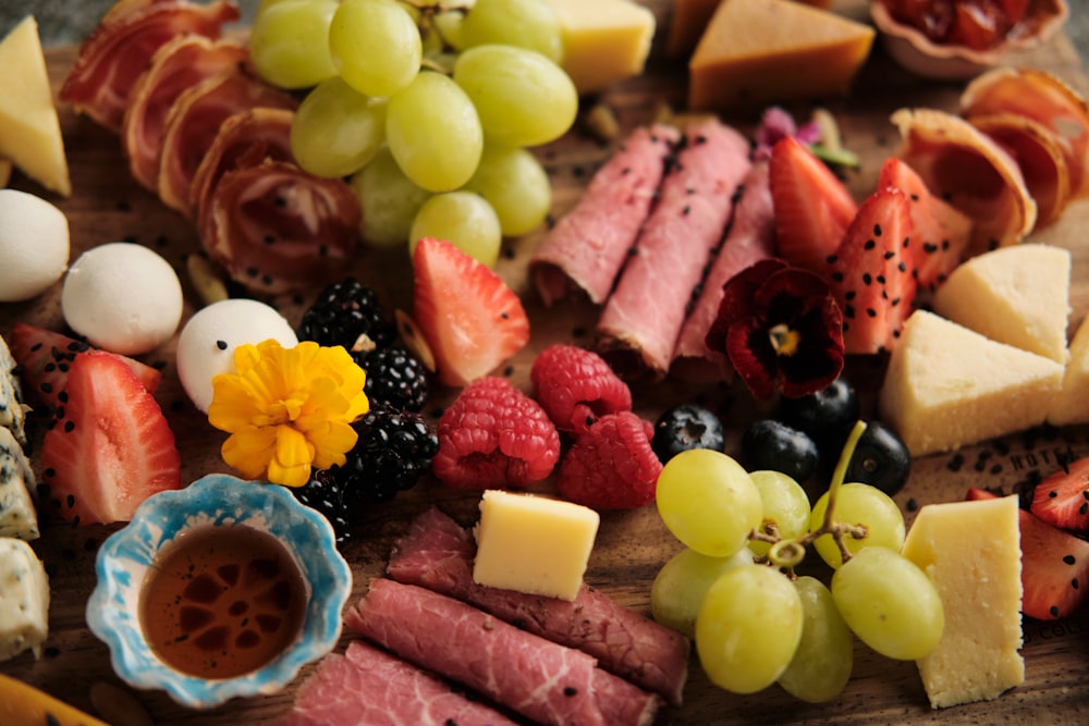 a variety of cheeses, meats, and fruit on a cutting board