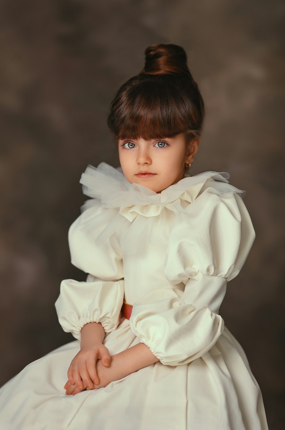 a little girl in a white dress sitting down