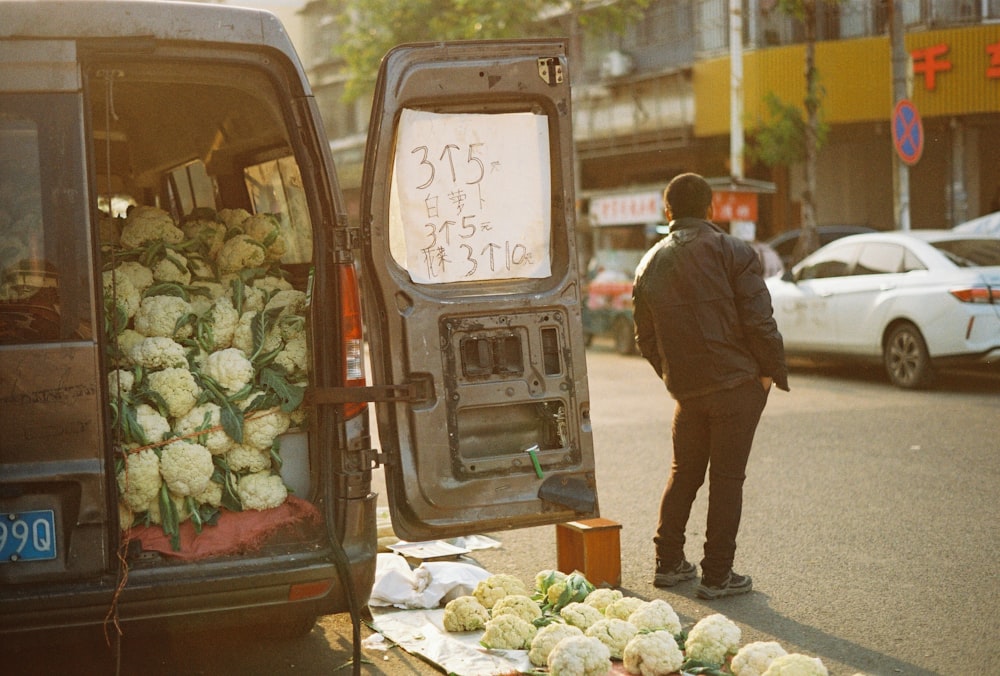 a man standing next to a van filled with vegetables